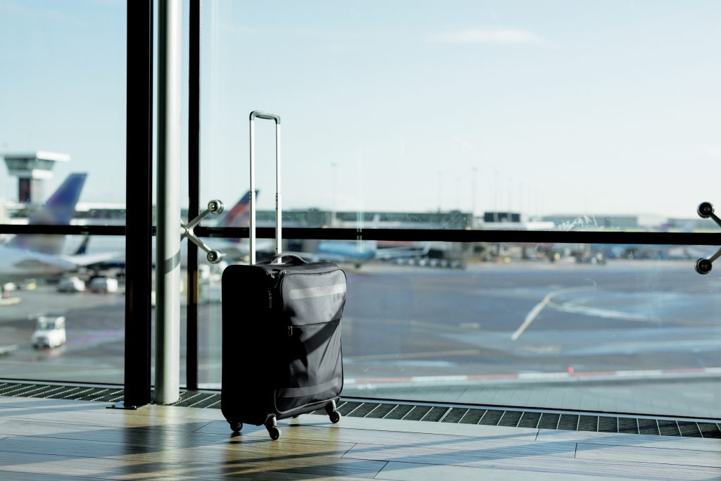 Ein Handkoffer steht verlassen auf einem Flughafen vor einer Glasfront.