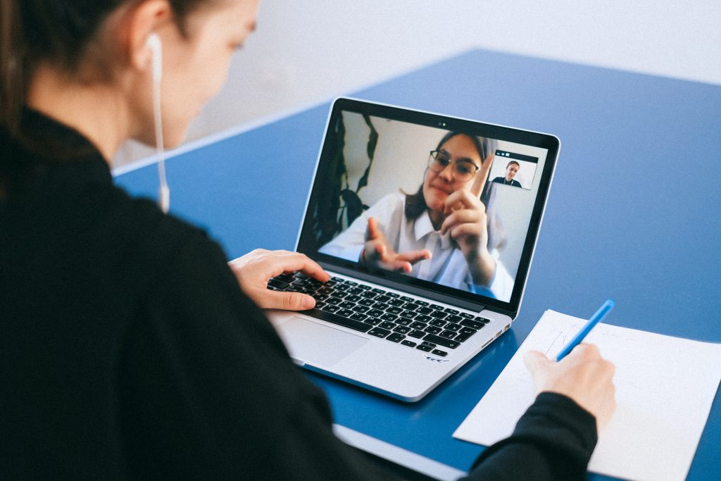 Frau sieht sich ein Onlinetraining auf einem Laptop an und schreibt auf einem Block Papier mit.